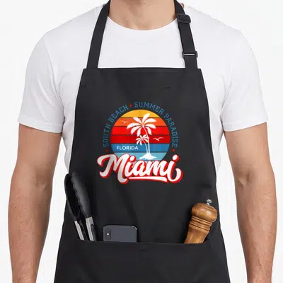 Tablier de cuisine noir avec logo vintage Miami palmier et texte South Beach Summer Paradise Florida en couleurs vives.