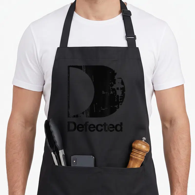 Tablier de cuisine noir avec une grande lettre D érodée et le mot Defected imprimé en dessous en typographie grunge.
