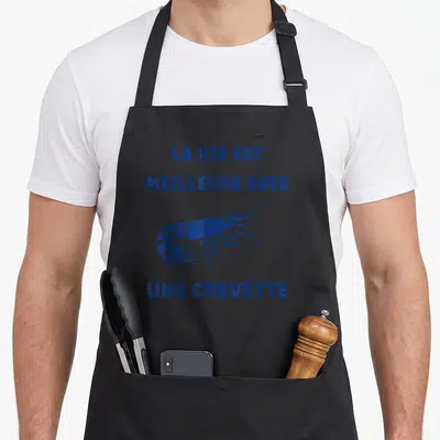 Tablier de cuisine noir avec une crevette bleue et le texte La vie est meilleure avec une crevette imprimé en lettres capitales.