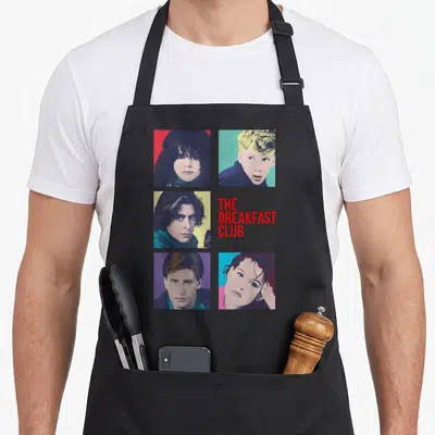 Tablier de cuisine noir avec cinq portraits colorés style pop art et le titre The Breakfast Club en rouge.