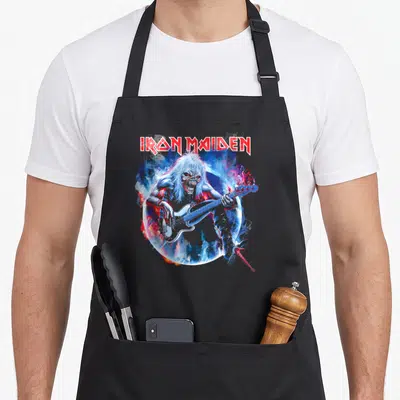 Tablier de cuisine noir avec Eddie d'Iron Maiden jouant de la basse entouré de fumée colorée.