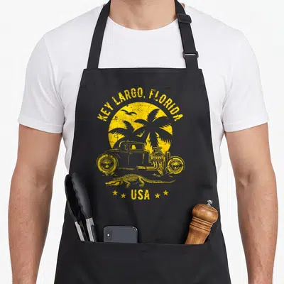 Tablier de cuisine noir avec illustration jaune d'un hotrod, palmier, crocodile et texte Key Largo Florida USA.