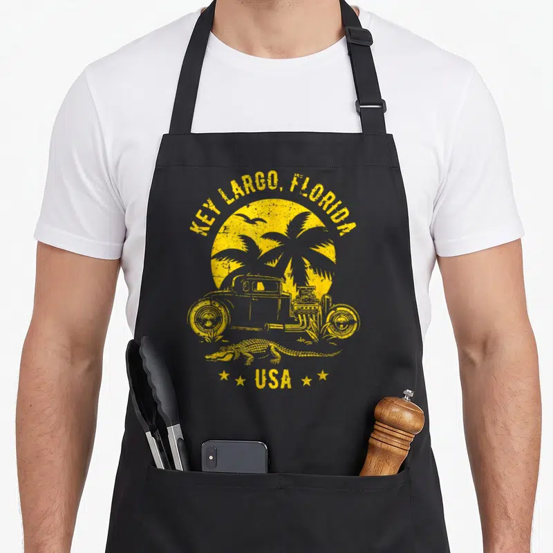 Tablier de cuisine noir avec illustration jaune d'un hotrod, palmier, crocodile et texte Key Largo Florida USA.