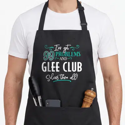 Tablier de cuisine noir avec le texte 99 problèmes et Glee Club les résout tous en blanc et turquoise.