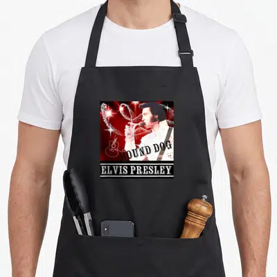 Tablier de cuisine noir avec une illustration colorée d'Elvis Presley chantant sous des étoiles lumineuses.