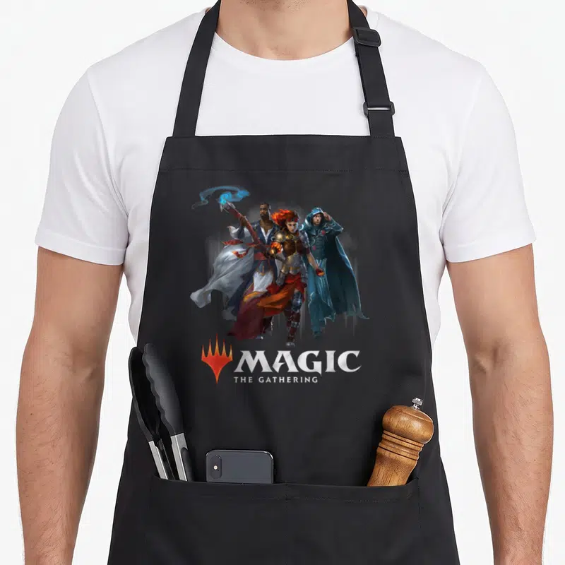 Tablier de cuisine noir avec l'illustration de trois personnages magiques et le logo Magic The Rassemblement en bas.