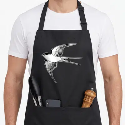 Tablier de cuisine noir avec une hirondelle stylisée en vol aux ailes déployées et queue fourchue, dessin noir et blanc.