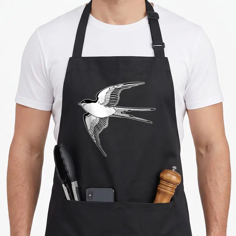 Tablier de cuisine noir avec une hirondelle stylisée en vol aux ailes déployées et queue fourchue, dessin noir et blanc.