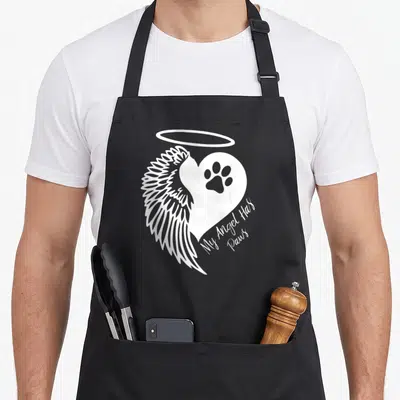 Tablier de cuisine noir avec motif blanc ailes, halo et patte dans un cœur portant l'inscription My Angel Has Paws.