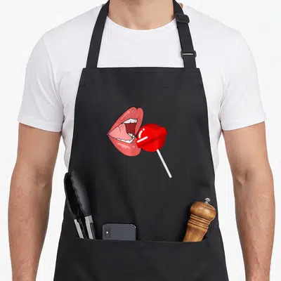 Tablier de cuisine noir avec illustration de lèvres roses ouvertes et d'une sucette rouge sur bâton blanc.