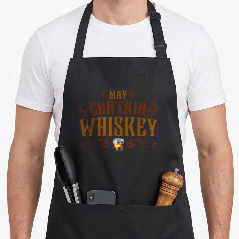 Tablier de cuisine noir avec inscription May Contain Whiskey et illustration de verre à whisky avec ice cube.