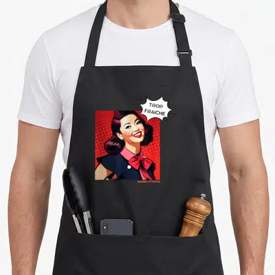 Tablier de cuisine noir avec illustration d'une femme aux cheveux noirs et bulle de dialogue Trop fraiche sur fond rouge à pois.