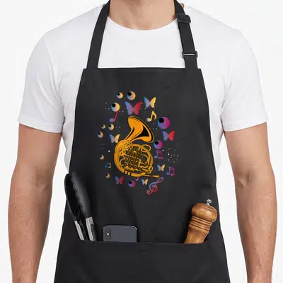 Tablier de cuisine noir avec une corne d'harmonie dorée, des papillons, des yeux et des notes de musique aux couleurs vives.