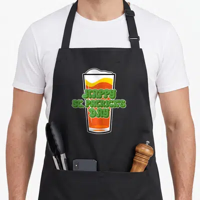 Tablier de cuisine noir avec illustration de verre de bière et texte Happy St. Patrick's Day en lettres vertes bulbeuses.