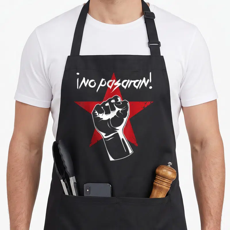 Tablier de cuisine noir avec poing levé blanc sur étoile rouge et inscription No Pasaran en lettres blanches stylisées.