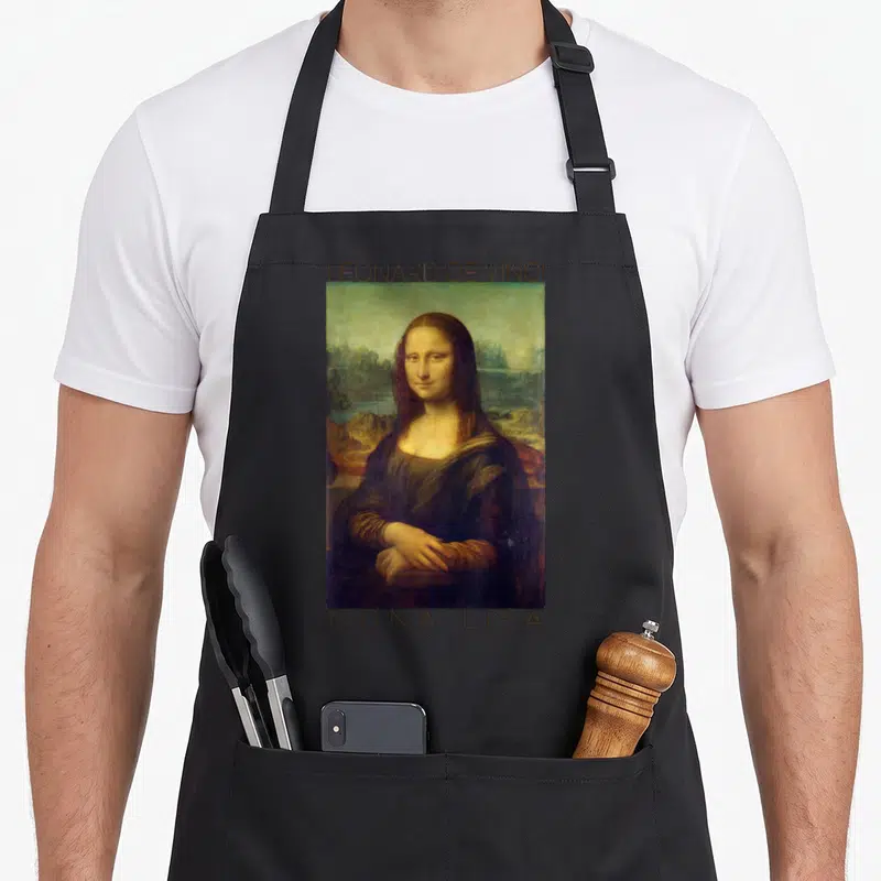 Tablier de cuisine noir avec reproduction de la Joconde et texte Leonard de Vinci Mona Lisa imprimé en haut et en bas du motif.