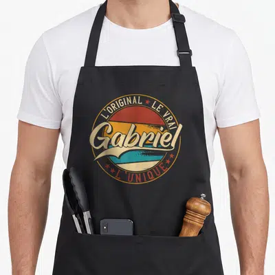 Tablier de cuisine noir avec logo circulaire vintage affichant le prénom Gabriel en lettres crème et des étoiles rouges.