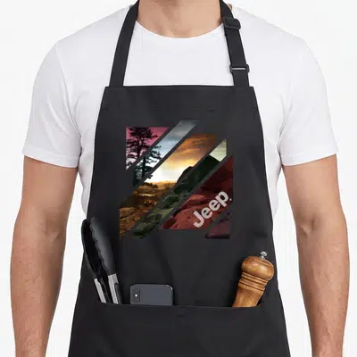 Tablier de cuisine noir avec motif géométrique diagonal montrant un véhicule sur terrain rocailleux et le logo Jeep stylisé.