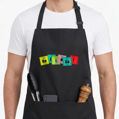 Tablier de cuisine noir avec cinq cases colorées représentant des éléments chimiques fantaisistes et le mot Bazinga.