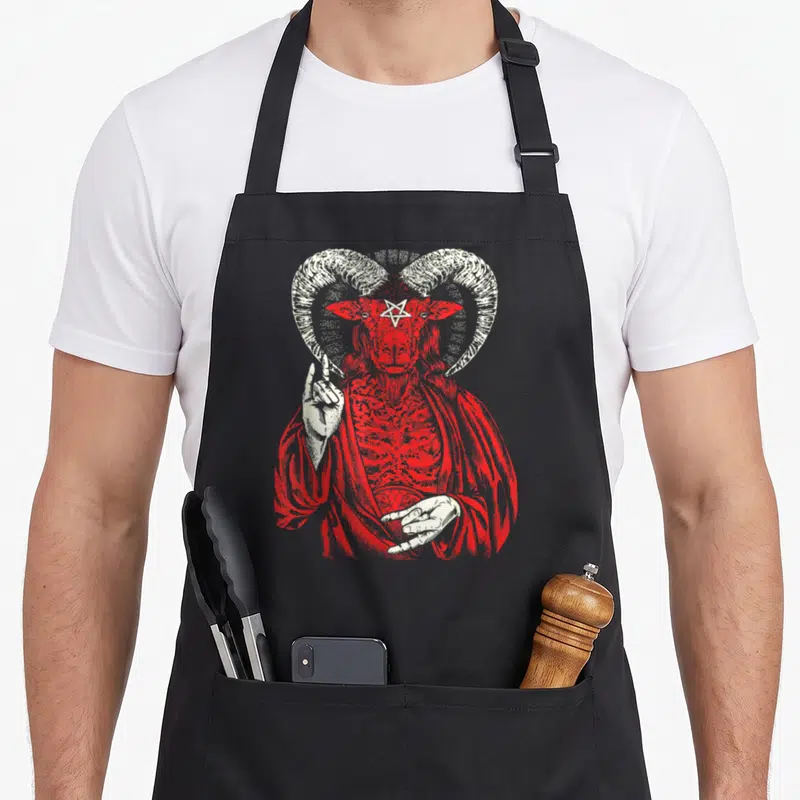 Tablier de cuisine noir avec illustration rouge et blanche représentant une figure démoniaque à grandes cornes et pentagramme sur le front.