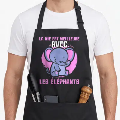 Tablier de cuisine noir avec un bébé éléphant bleu souriant et le texte La vie est meilleure avec les éléphants en rose et blanc.