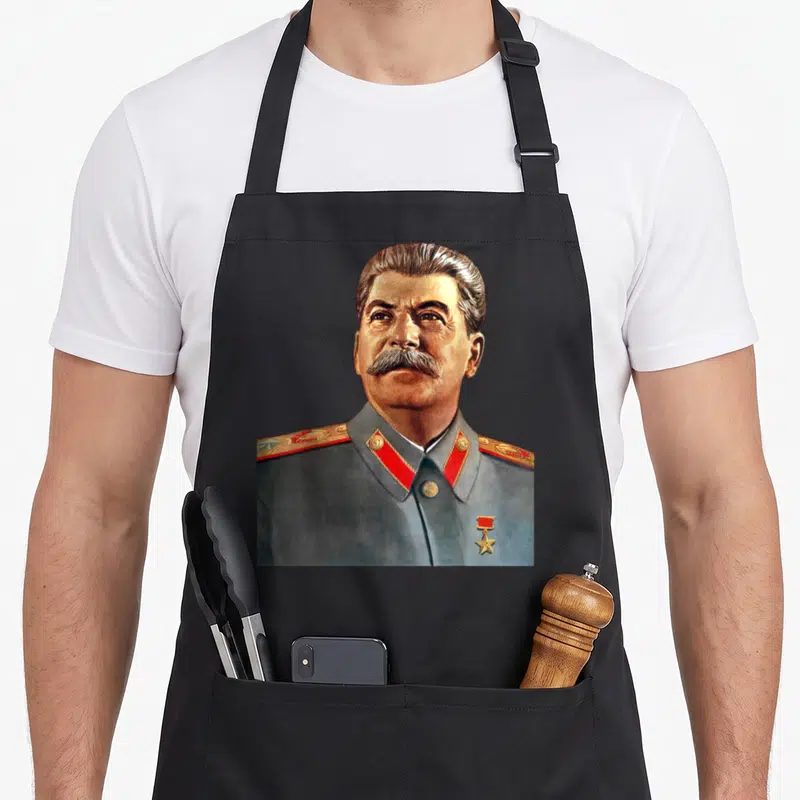 Tablier de cuisine noir avec portrait couleur de Staline en uniforme gris, épaulettes rouges et médaille dorée sur la poitrine.