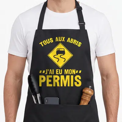Tablier de cuisine noir avec une illustration de panneau de glissade jaune et du texte humoristique sur la conduite.