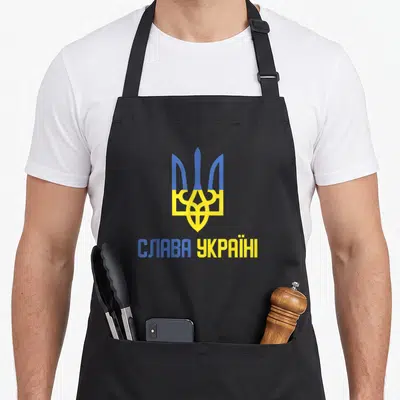 Tablier de cuisine noir orné d'un trident bleu et jaune surmontant l'inscription en lettres capitales.