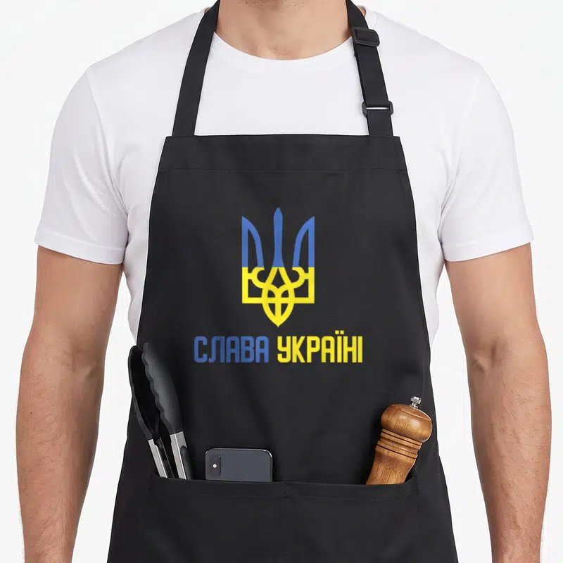 Tablier de cuisine noir orné d'un trident bleu et jaune surmontant l'inscription en lettres capitales.