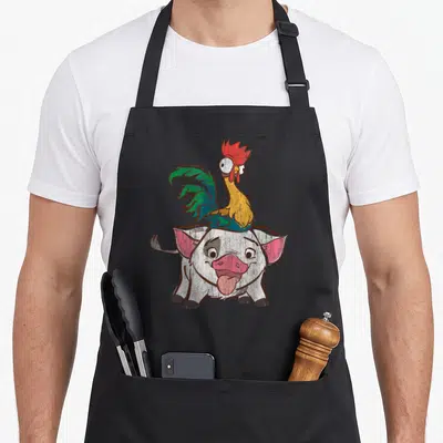Tablier de cuisine noir avec illustration colorée du coq Hei Hei sur le cochon Pua aux yeux exorbités.