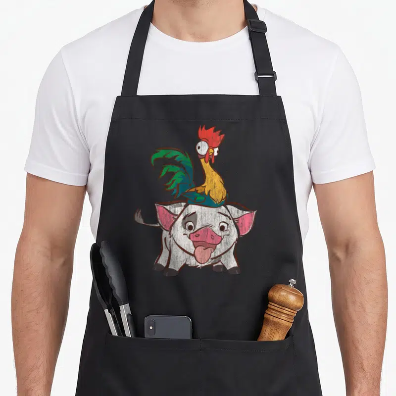 Tablier de cuisine noir avec illustration colorée du coq Hei Hei sur le cochon Pua aux yeux exorbités.