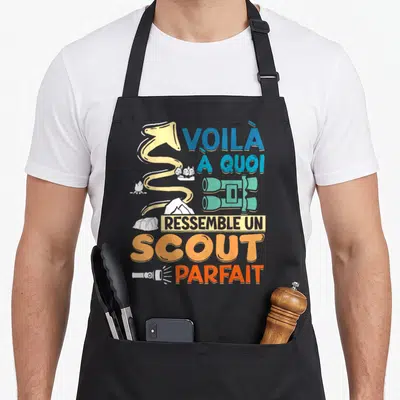 Tablier de cuisine noir avec illustration de boussole, tente, jumelles et texte orange bleu.
