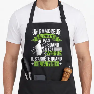 Tablier de cuisine noir avec silhouette blanche d'un ramoneur portant une échelle et texte blanc et vert sur fond uni.