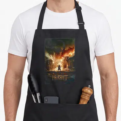 Tablier de cuisine noir avec illustration du Hobbit face au dragon Smaug dans une ville en ruine.