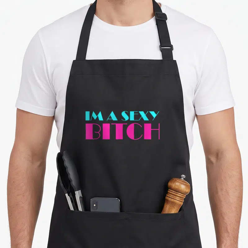 Tablier de cuisine noir avec inscription IM A SEXY BITCH en lettres bleues et roses vives.