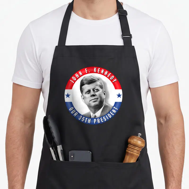 Tablier de cuisine noir avec badge circulaire JFK John F. Kennedy Our 35th President portrait noir et blanc étoiles bleues.