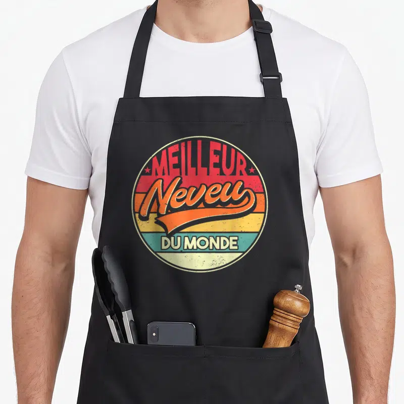 Tablier de cuisine noir avec un logo rond coloré affichant Meilleur Neveu Du Monde en typographie vintage.