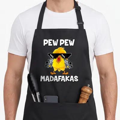 Tablier de cuisine noir avec un poussin jaune portant des lunettes de soleil pixelisées et tenant deux revolvers gris.