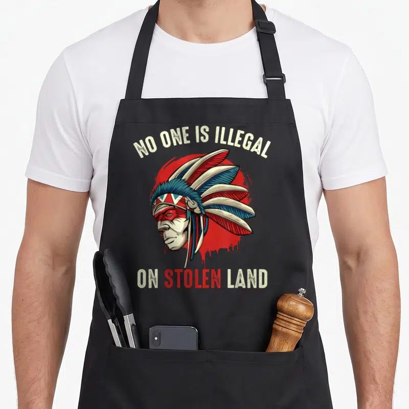 Tablier de cuisine noir avec illustration d'un chef amérindien et texte No One Is Illegal On Stolen Land sur fond rouge.