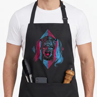 Tablier de cuisine noir avec illustration colorée de Harley Quinn aux cheveux bicolores et texte Pudd sous le visage.