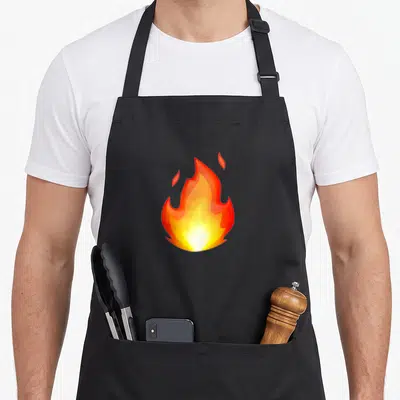 Tablier de cuisine noir orné d'une grande illustration de flamme orange et jaune vif au centre du torse.