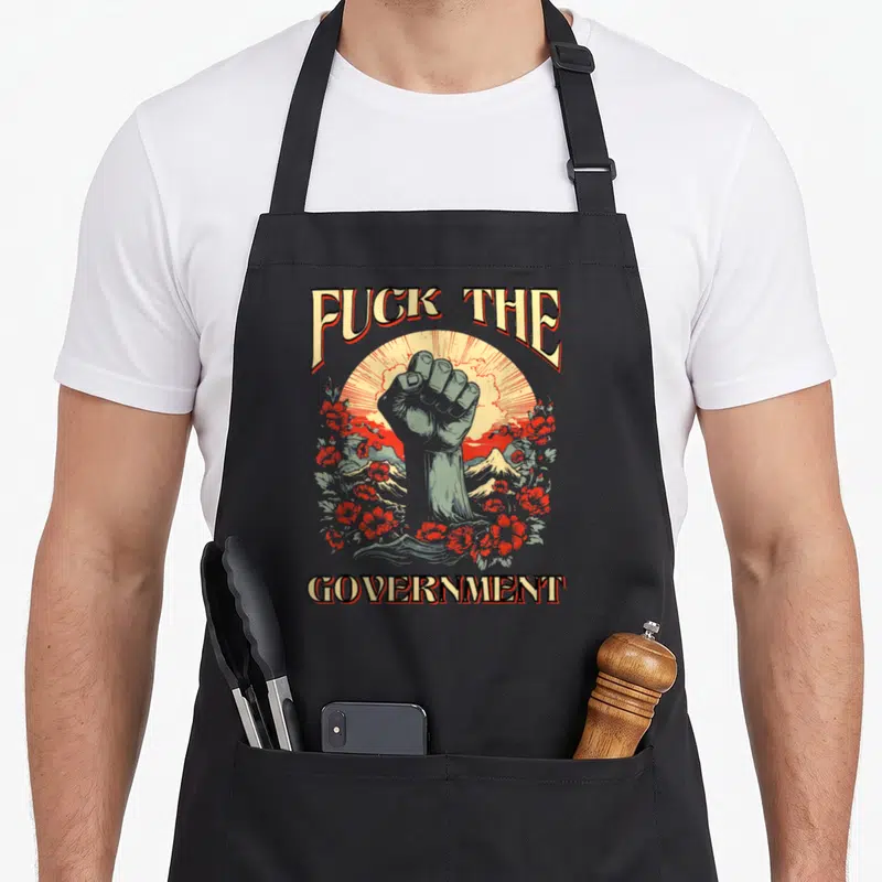 Tablier de cuisine noir avec un poing levé, des fleurs rouges et les mots Fuck The Government en typographie vintage.