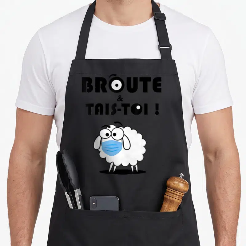 Tablier de cuisine noir avec un mouton blanc portant un masque chirurgical bleu sous le texte broute et tais-toi