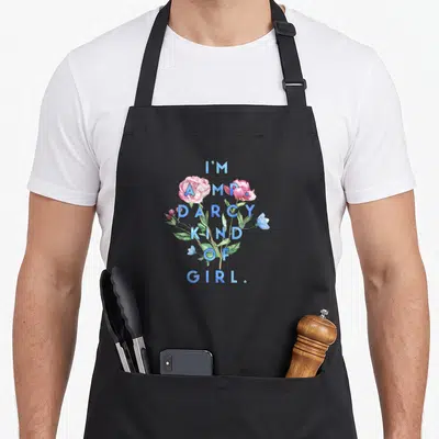 Tablier de cuisine noir avec texte bleu J'adore M. Darcy Kind of Girl entouré de fleurs roses et de feuilles vertes.
