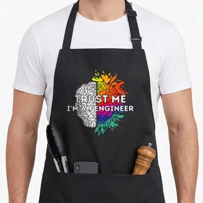 Tablier de cuisine noir avec illustration d'un cerveau divisé en gris et couleurs vives portant l'inscription Trust me I'm an Engineer.