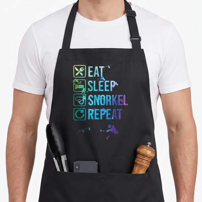 Tablier de cuisine noir avec l'inscription Eat Sleep Snorkel Repeat en dégradé bleu et vert accompagnée d'icônes stylisées.