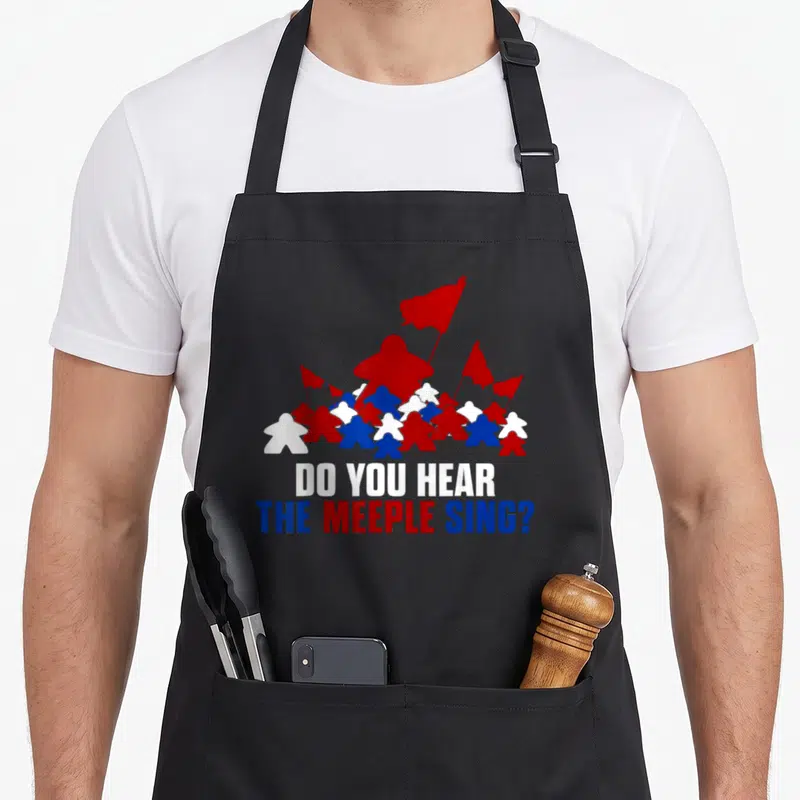 Tablier de cuisine noir avec des meeple rouges blancs et bleus portant des drapeaux et le texte Do You Hear The Meeple Sing.