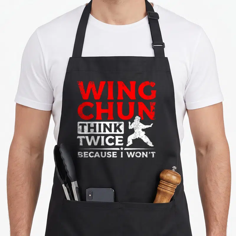 Tablier de cuisine noir avec le texte Wing Chun pense deux fois et une silhouette de combattant en position de garde.