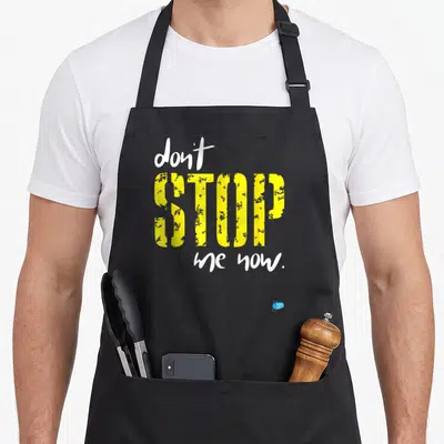 Tablier de cuisine noir avec l'inscription Don't Stop Me Now en typographie jaune et blanche.