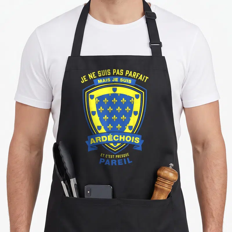 Tablier de cuisine noir avec un blason bleu et jaune portant les mots Je ne suis pas parfait mais je suis Ardéchois et c'est presque pareil.